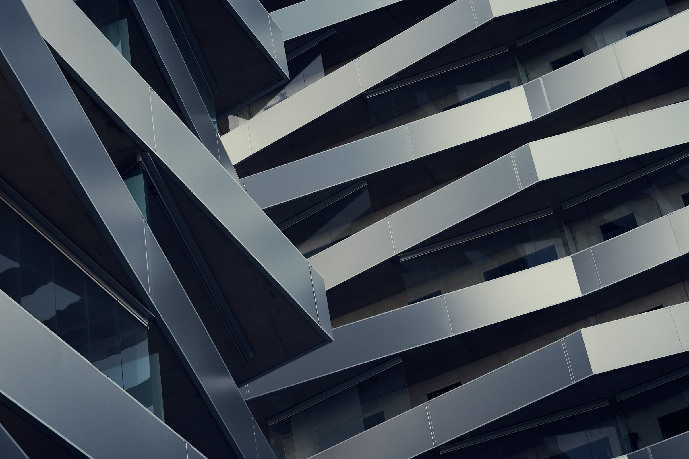 Close-up view of a modern building facade with angled, overlapping metal beams and glass windows, creating a geometric, abstract pattern—reminiscent of the clean lines and structural clarity found in well-designed software architecture using Java and ArchUnit.