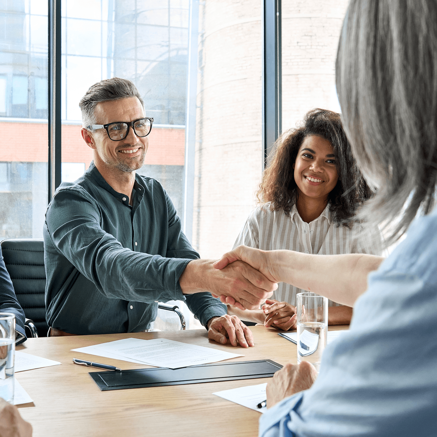 Happy businessman and businesswoman shaking hands at group board meeting.