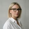 Woman with straight blonde hair and glasses, wearing a white shirt, looking at the camera against a plain, light-colored background—Agnieszka Orłowska exudes calm confidence in this simple yet striking portrait.