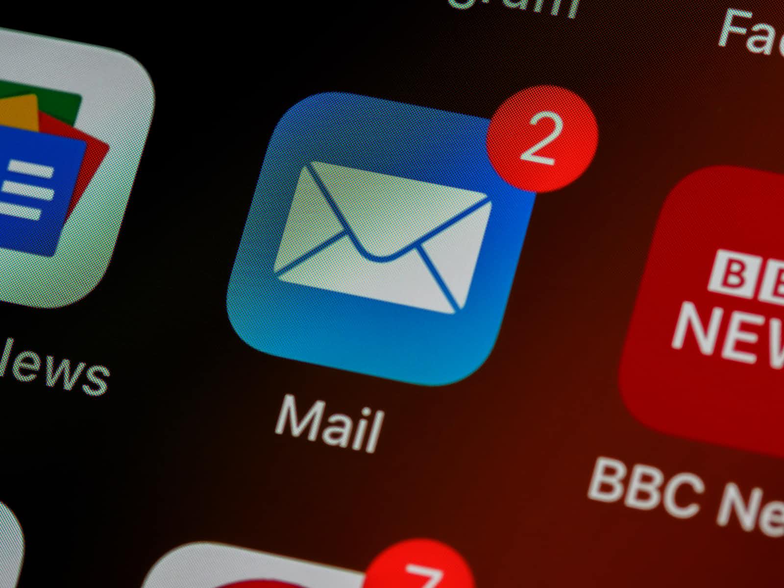 Close-up of a smartphone screen showing the Mail app icon with a red notification badge displaying the number 2, indicating two unread emails. Other app icons are partially visible around it, highlighting the importance of reliable communication—much like implementing the Transactional Outbox Pattern to ensure messages aren’t missed.