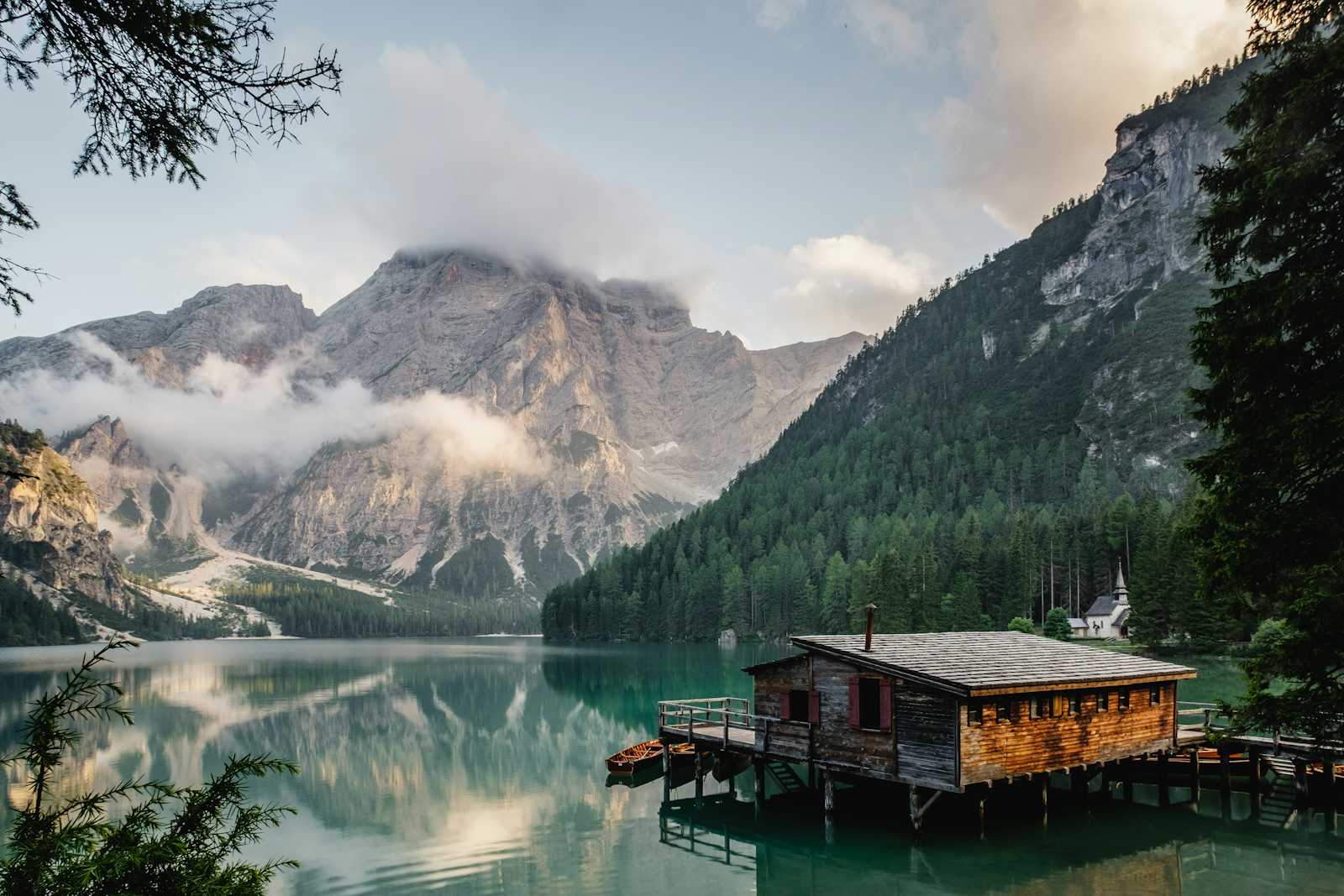 A wooden lakehouse cabin on stilts stands over a calm mountain lake, surrounded by pine forests, with tall rocky mountains and clouds in the background. This tranquil retreat evokes both serenity and a sense of securing peaceful data access amidst nature’s grandeur.