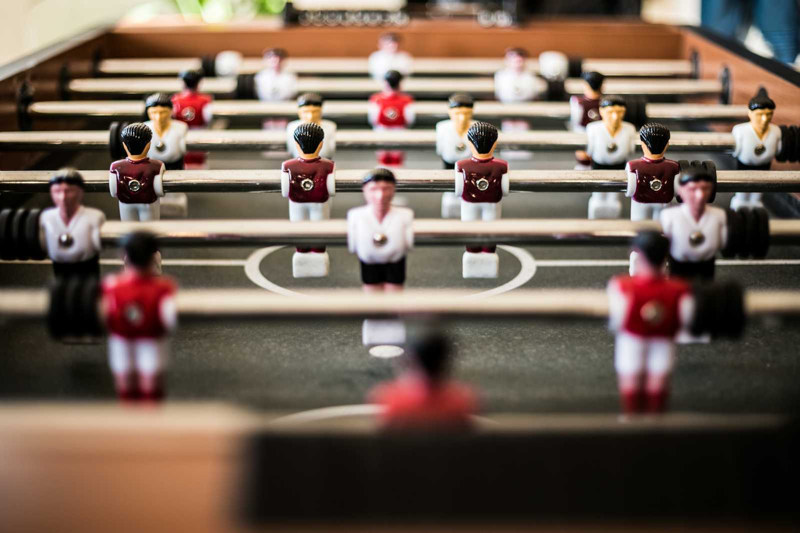 Close-up of a foosball table with teams of red and white player figures positioned on rods over a green playing field, reminiscent of enabling teams collaborating seamlessly—much like effective team topologies in test automation.