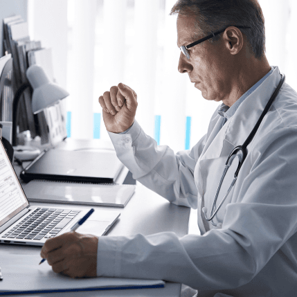 Serious mature doctor physician using laptop tech in hospital office. Senior middle aged male gp checking patient clinical registration form, elearning working looking at computer sitting at desk.