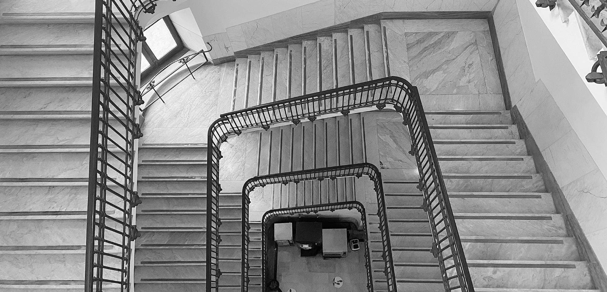 High-angle view of a multi-story square marble staircase with dark metal railings, designed with the precision of autonomous engineering.